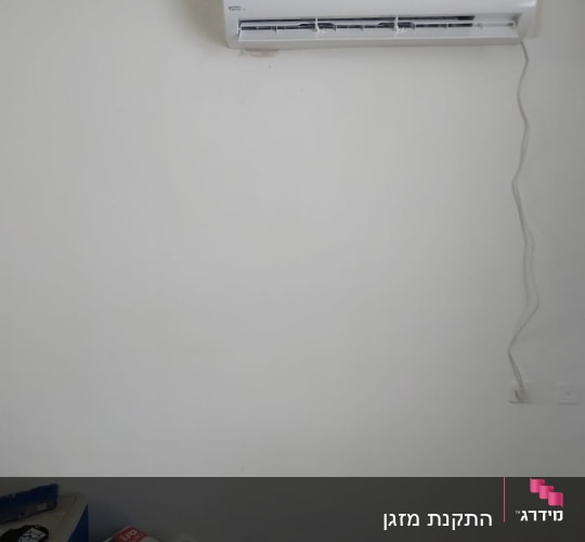מזגן מותקן על קיר לבן עם כבל חשמל